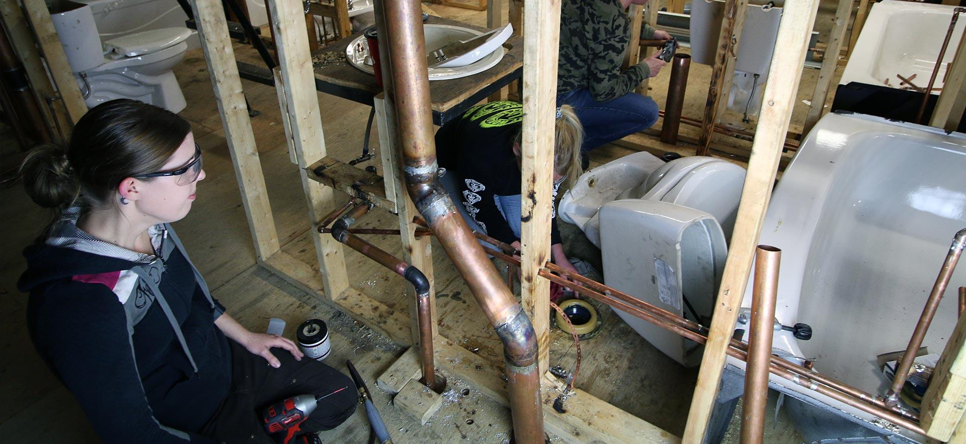 Female plumbing students work on in-class plumbing assignment as о. 