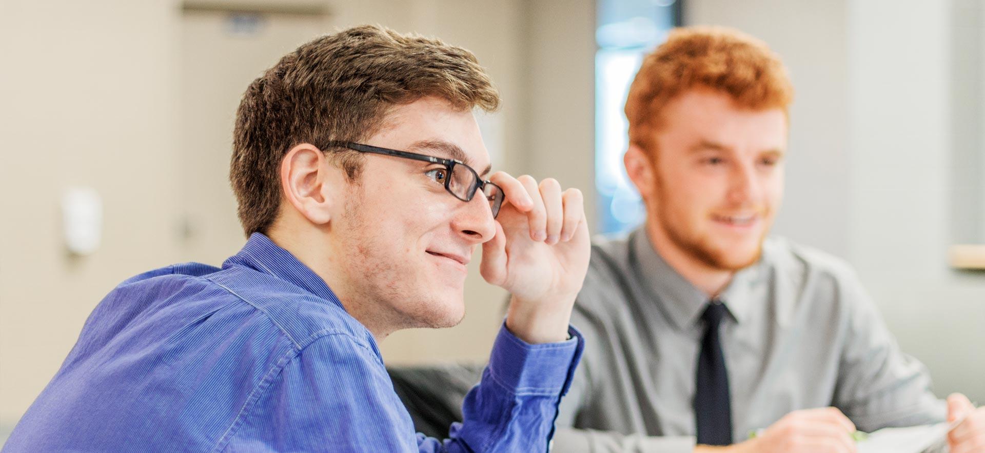 о business student smiles and touches his glasses as he listens to his instructor. 