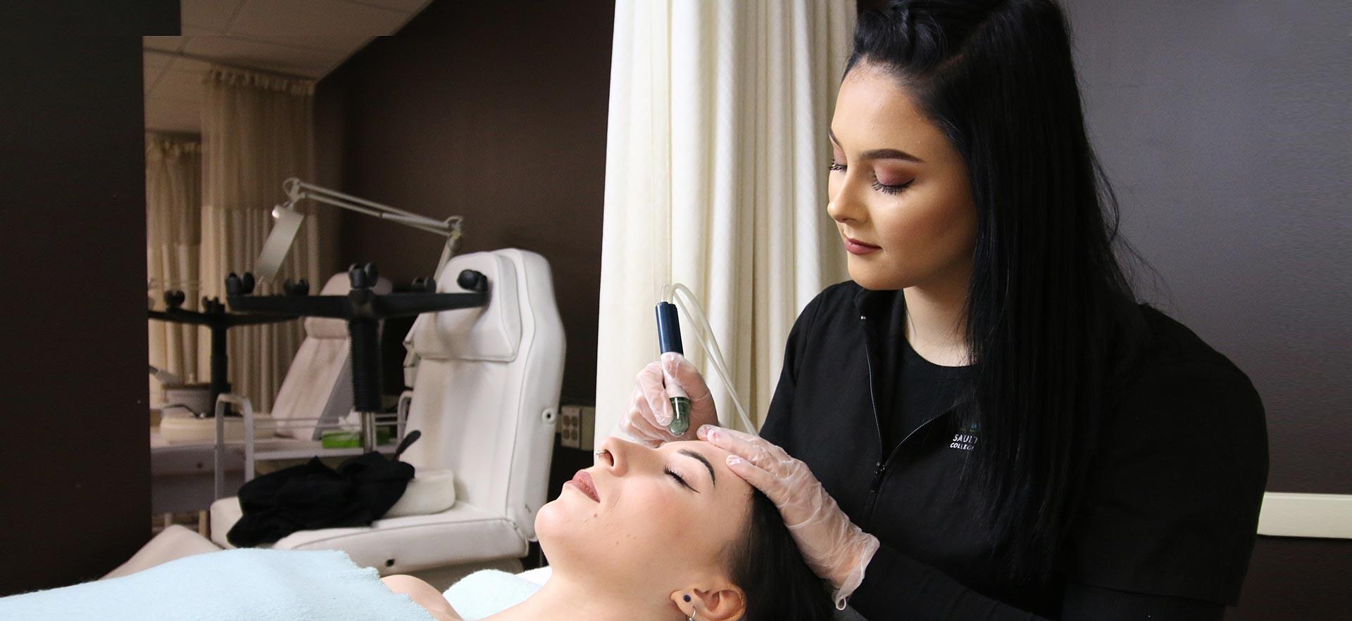 One female Esthetician student applies a skin treatment to another student in the о salon spa.