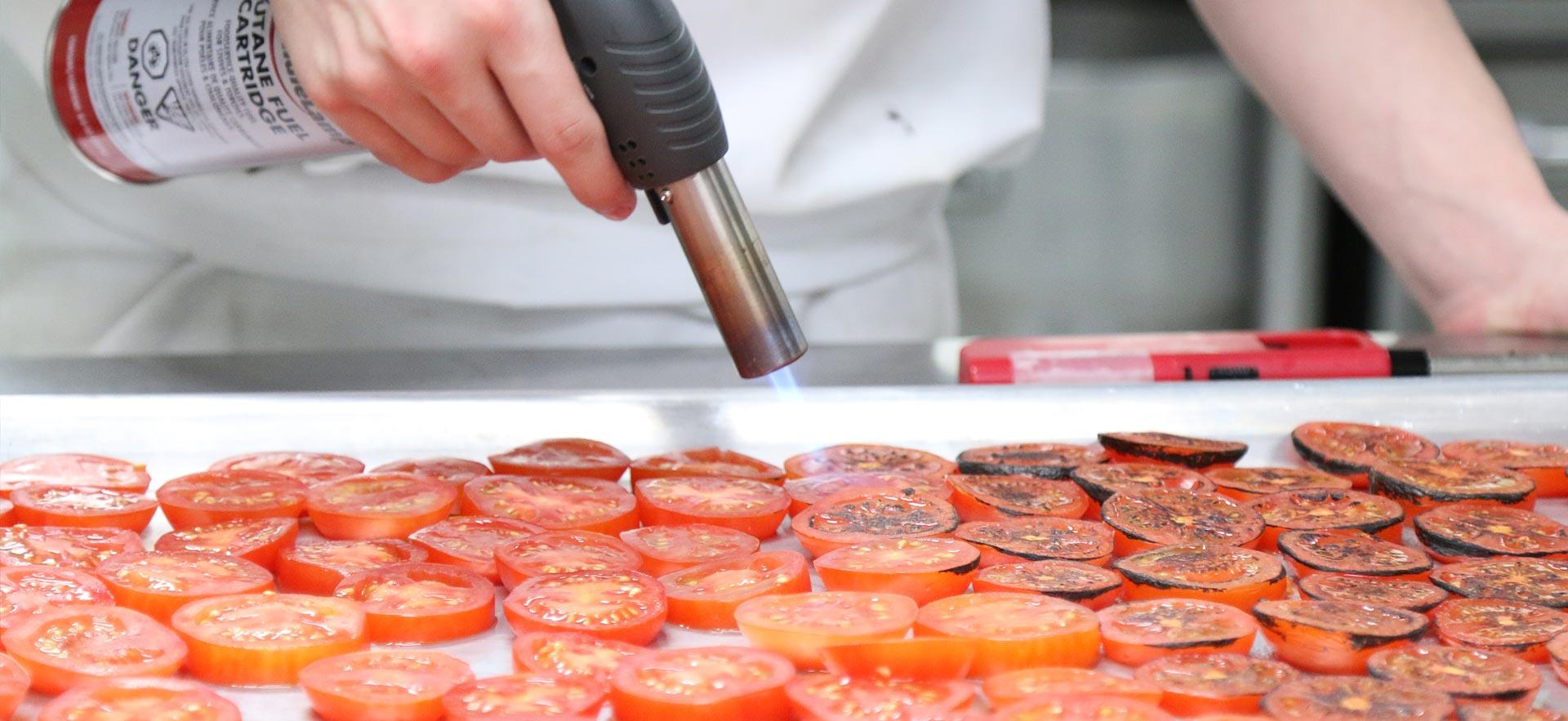 A culinary student fire roasting tomatoes in one the о culinary kitchens.