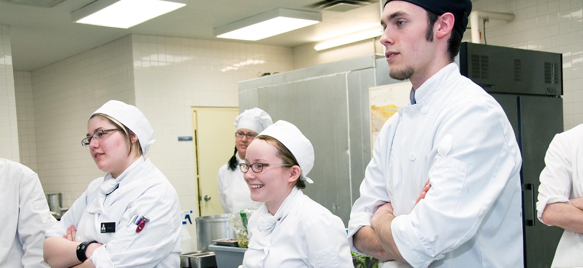 A group of culinary students listen to their instructor in one the о culinary kitchens.