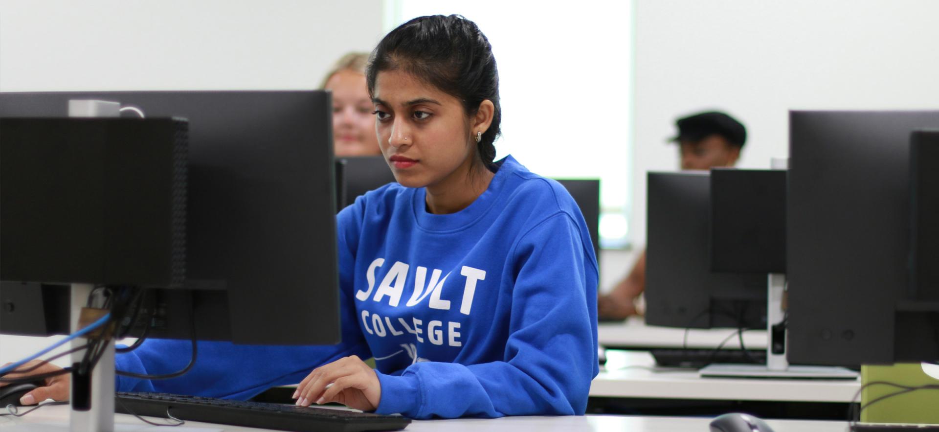 Student sitting at computer in class wearing blue о sweater